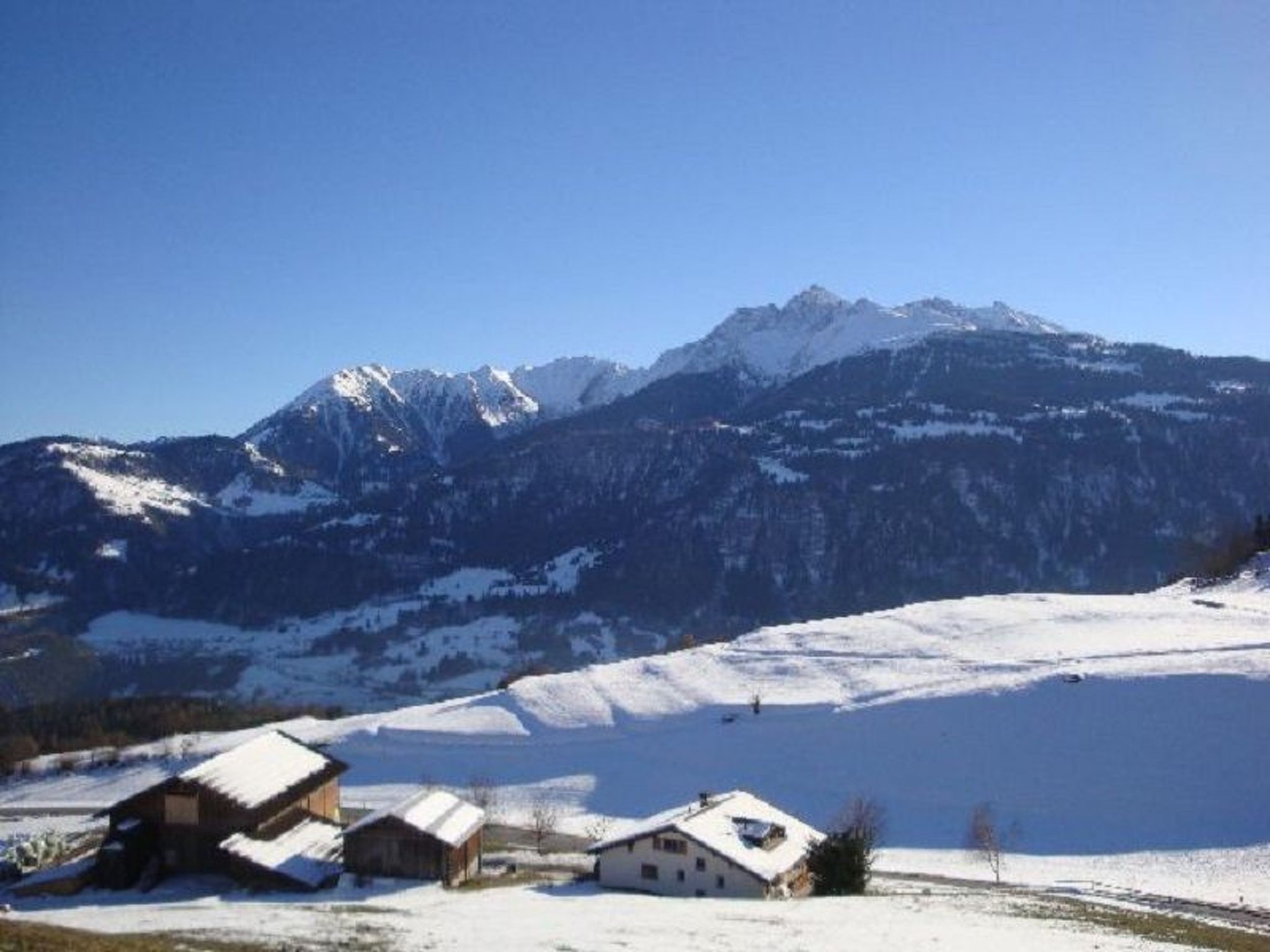 A mountainous landscape with snow-covered peaks and a small cluster of buildings in the foreground.