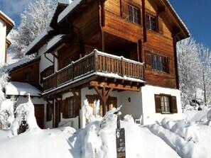 Een houten chalet met een balkon, omringd door sneeuwtakken.