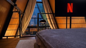 A bedroom with a large window, a bed, and a TV displaying the Netflix logo. - Cabana Industrial com Hidro e Piscina Aquecida (Palhoça)