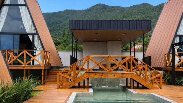 A modern house with a swimming pool, wooden deck, and a bridge connecting two sections. - Cabana Industrial com Hidro e Piscina Aquecida (Palhoça)