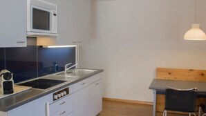 Moderni keittiö, jossa on mikroaaltouuni, pesuallas ja liesi, sekä puinen ruokapöytä ja riippuvalaisin.
