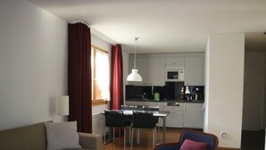 Olohuoneessa on sohva, nojatuoli, lasinen sohvapöytä sekä keittiöalue, jossa on ruokapöytä ja tuolit.
