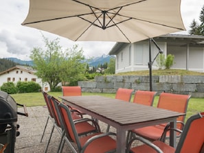 Eine Terrasse im Freien mit Tisch, Stühlen, einem Grill und einem großen Sonnenschirm.