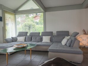 Ein modernes Wohnzimmer mit einem Ecksofa, einem Glastisch und Blick ins Grüne.