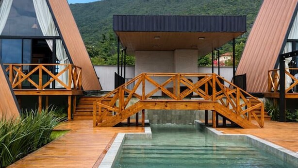 A modern building with a pool, wooden deck, and a bridge connecting two sections. - Cabana Country Romântica com Banheira & Piscina (Palhoça)
