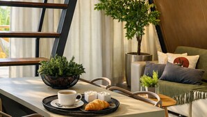 A modern living room with a sofa, a coffee table, a dining table with a plant, a croissant, and a cup of coffee. - Cabana Country Romântica com Banheira & Piscina (Palhoça)