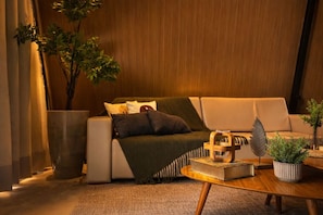 A modern living room with a sofa, a coffee table, a potted plant, and a bookshelf.
