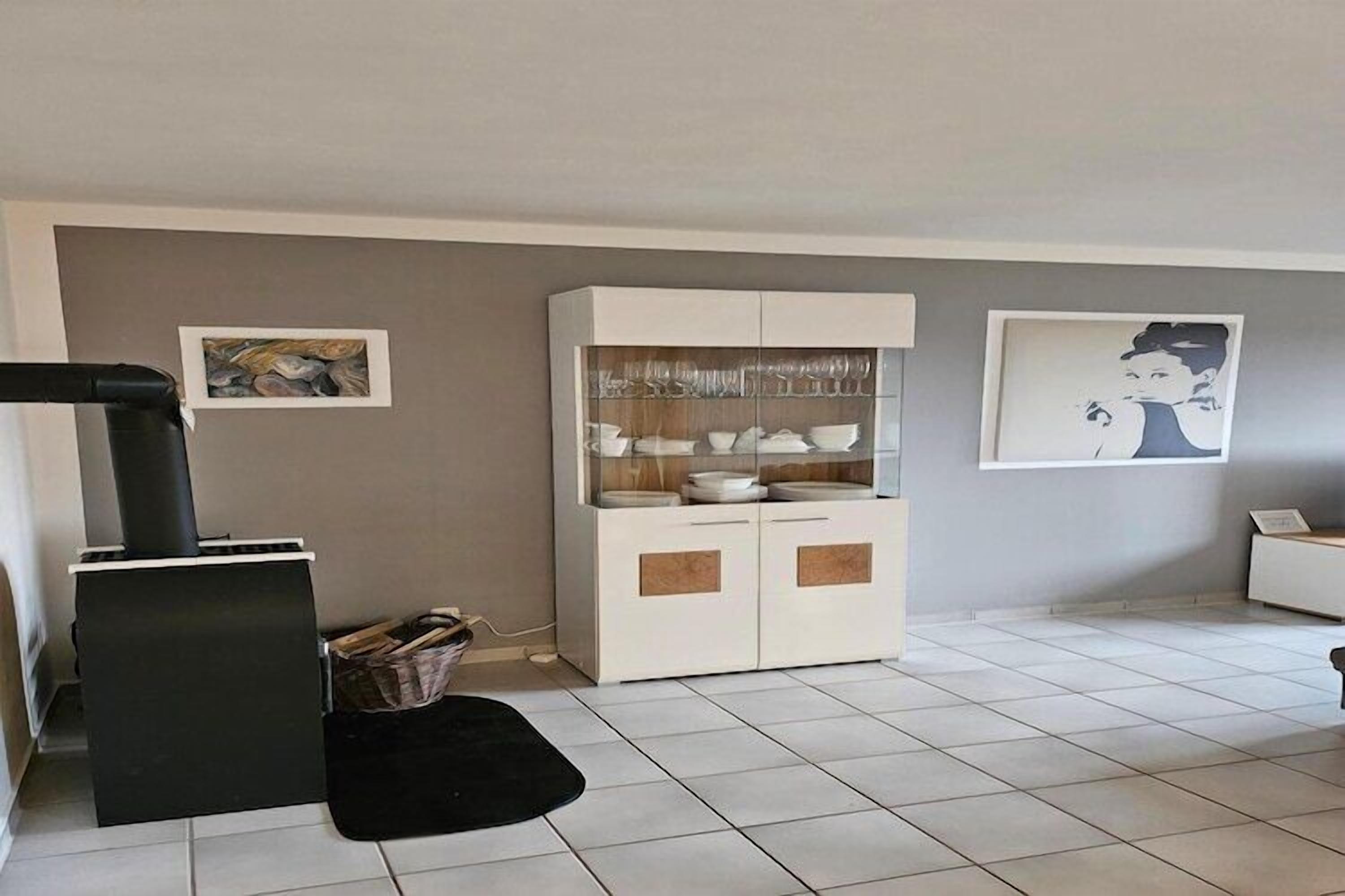 Ein Wohnzimmer mit Kamin, einer Vitrine mit Gläsern und zwei gerahmten Bildern an der Wand.