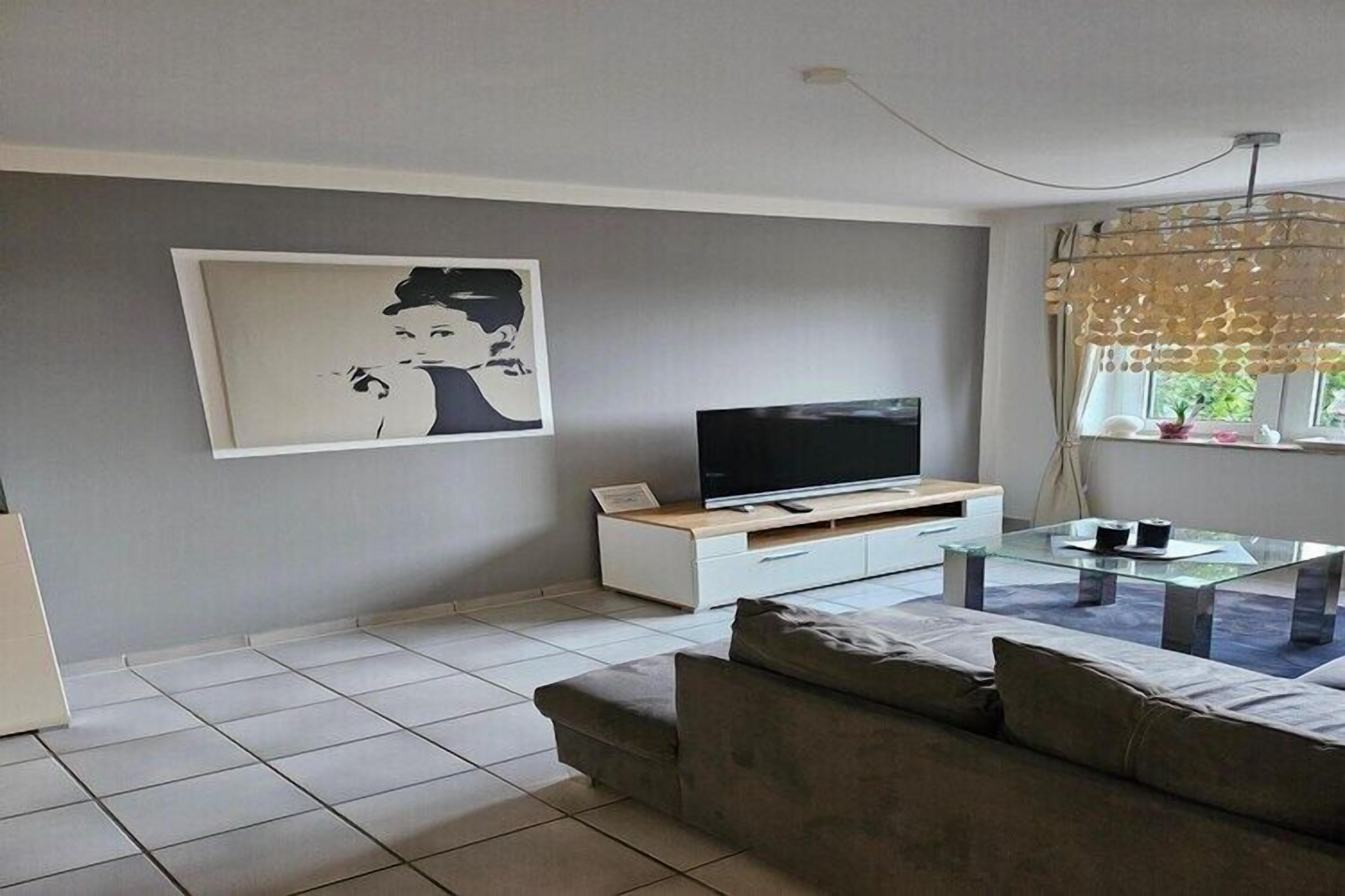 Un salon avec un téléviseur  à écran plat, un canapé, une table basse en verre et un tableau accroché au mur.
