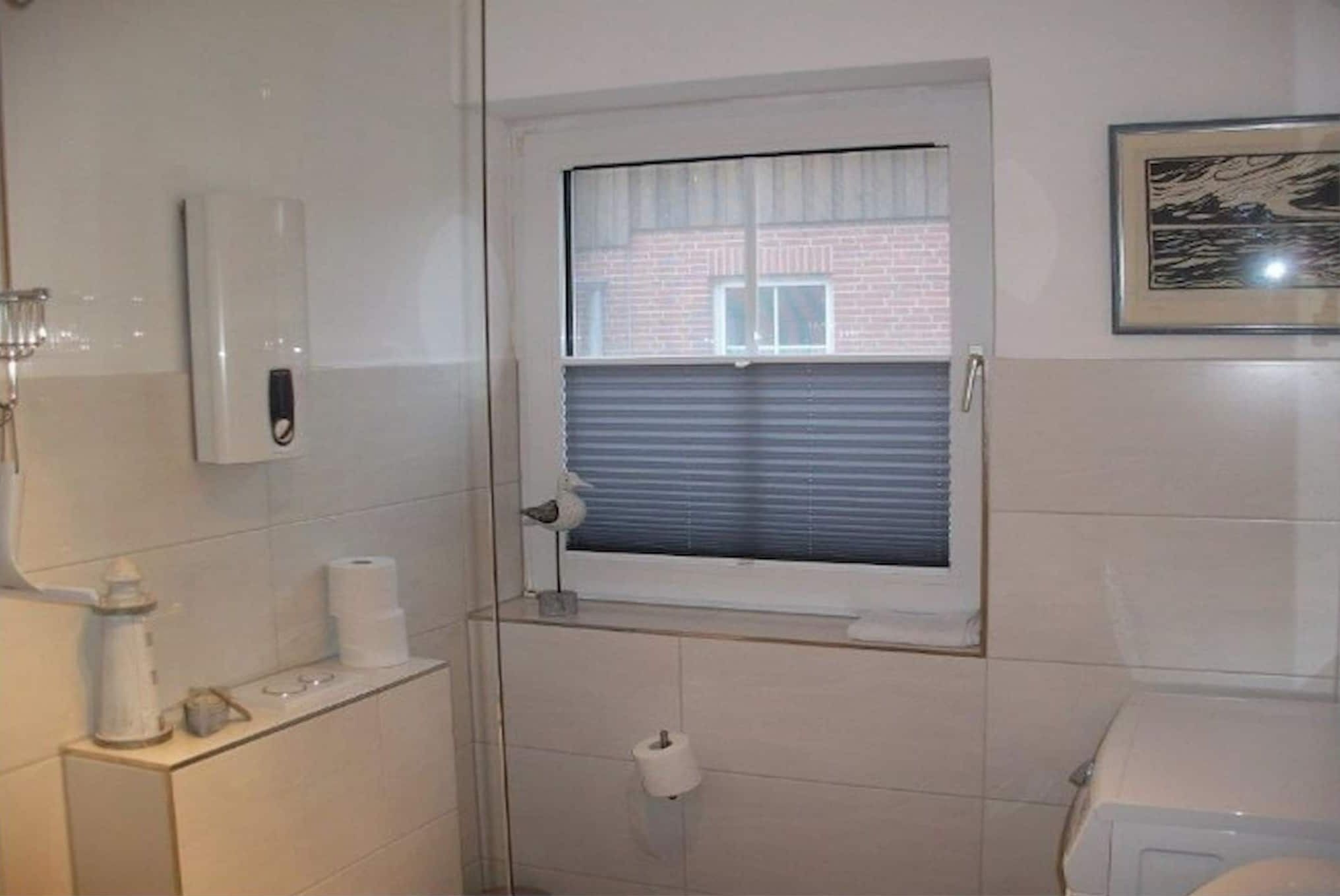 Un baño con inodoro, una ventana pequeña con persianas, un dispensador de toallas y un cuadro en la pared.