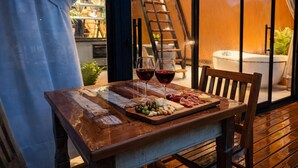 A wooden table with a cheese board, two glasses of red wine, and a wooden chair. - Cabana Praiana - Vivendas Ferreira (Palhoça)