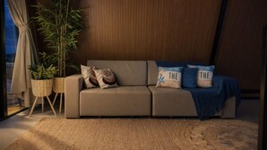 A modern living room with a sofa, two potted plants, and decorative pillows. - Cabana Praiana - Vivendas Ferreira (Palhoça)