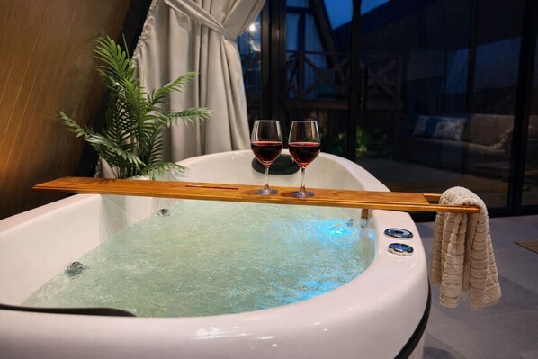 A hot tub with two glasses of red wine, a wooden tray, and a towel.