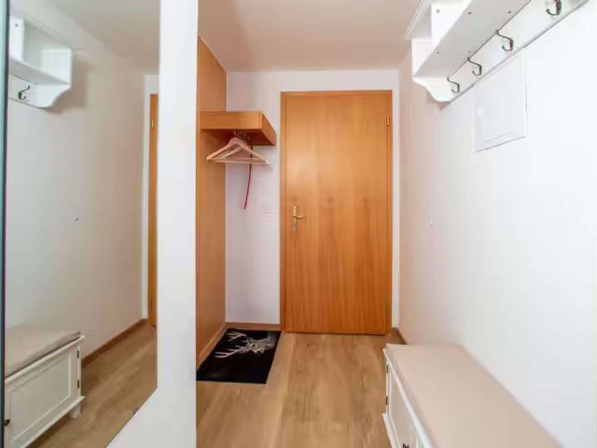 Un couloir étroit avec une porte en bois, un porte-manteau et un petit tapis.