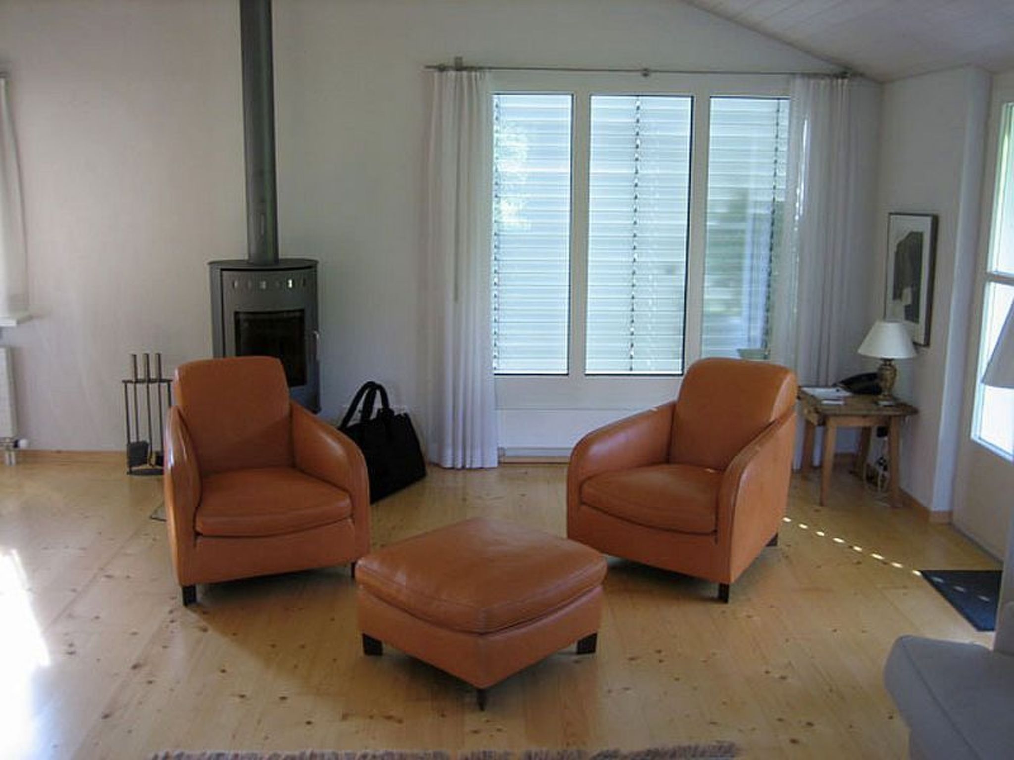 A living room with two leather armchairs, a small ottoman, a fireplace, and a window with blinds.