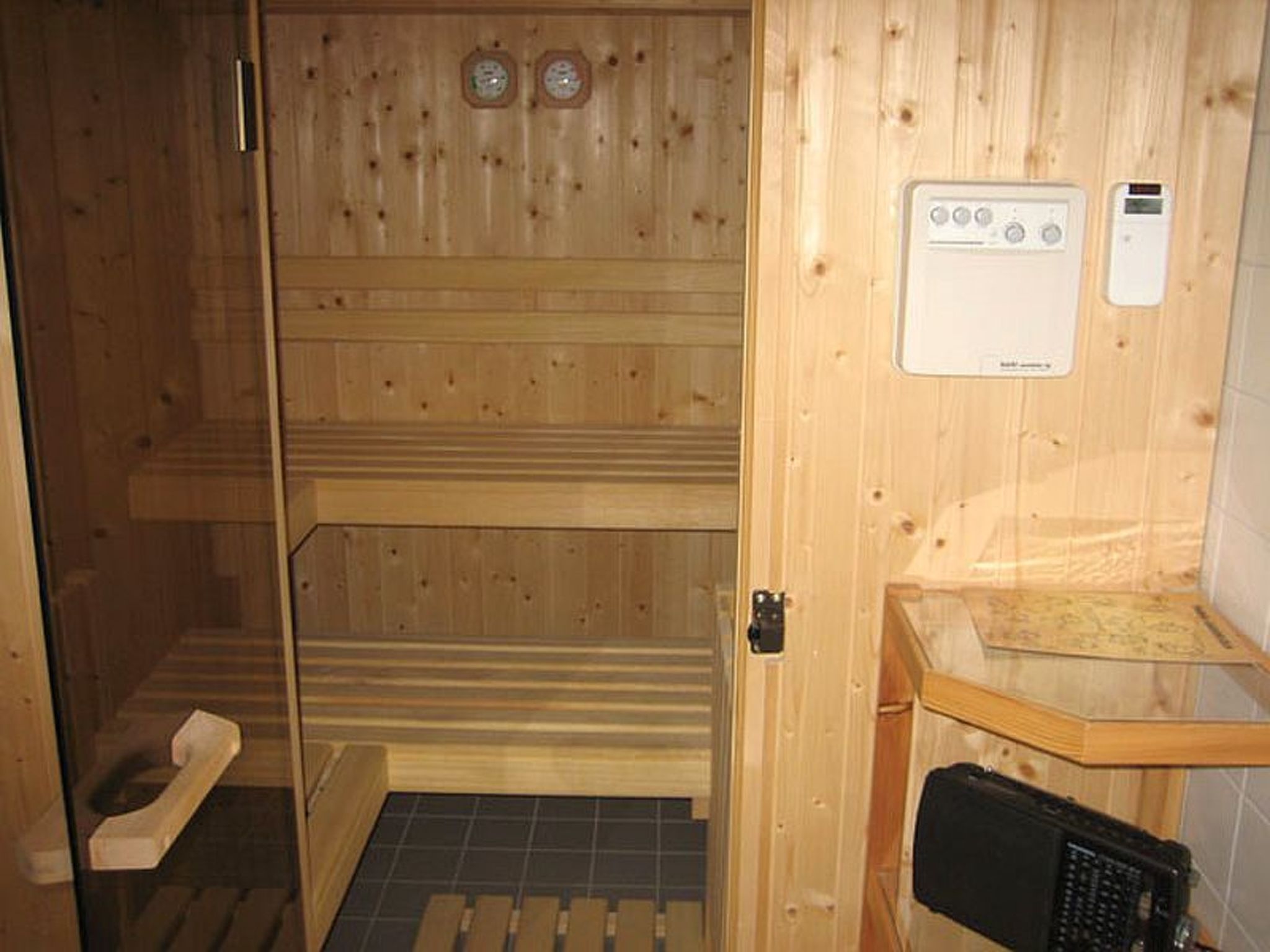 Una sala de sauna con paredes de madera, un banco, un panel de control y una pequeña mesa con una toalla.