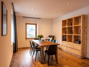 A dining area with a wooden table and chairs, a window with a view, and a built-in wooden shelving unit. - Flem Mountain Lodge, (Flims Waldhaus), by Interhome (Flims)