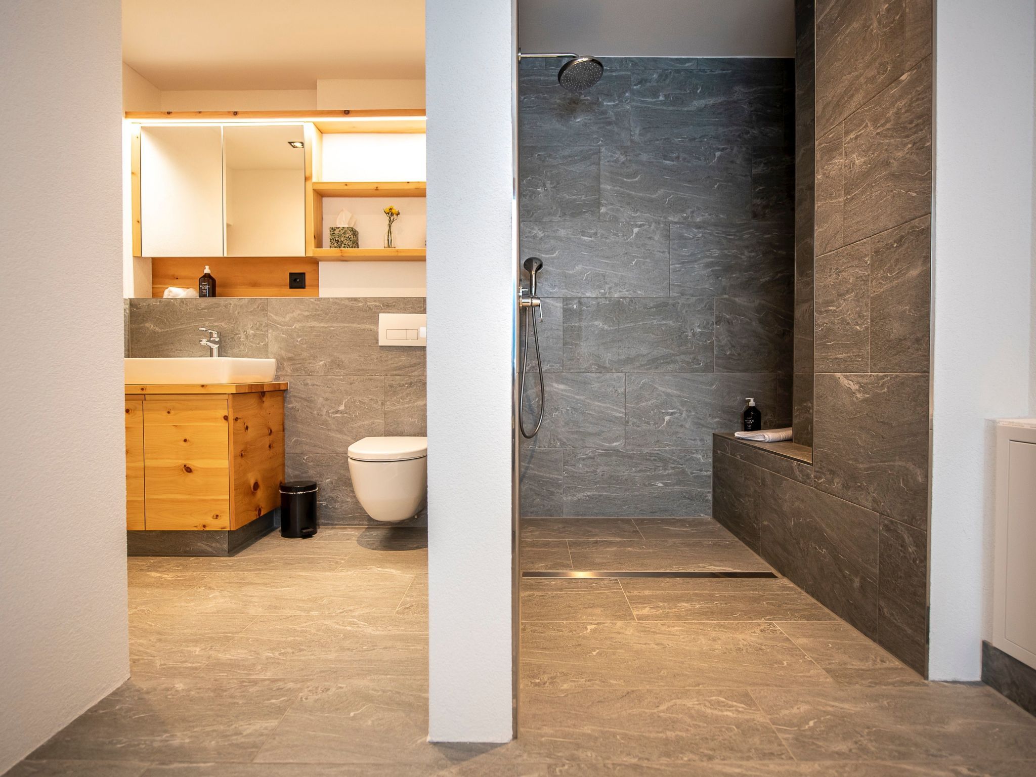 A modern bathroom with a shower, toilet, and wooden vanity.