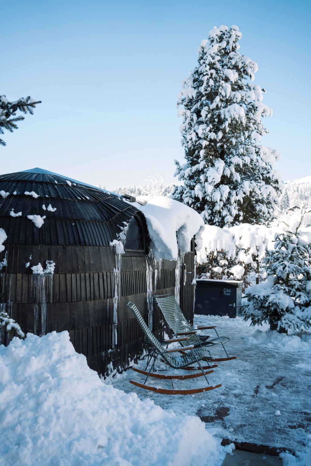 A snow-covered outdoor area with a wooden structure, a snow-covered tree, and a sled.