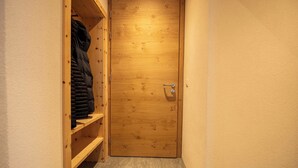 A wooden door with a metal handle, a wooden shelf with a black jacket, and a pair of shoes on the floor. - Flem Mountain Lodge, (Flims Waldhaus), by Interhome (Flims)