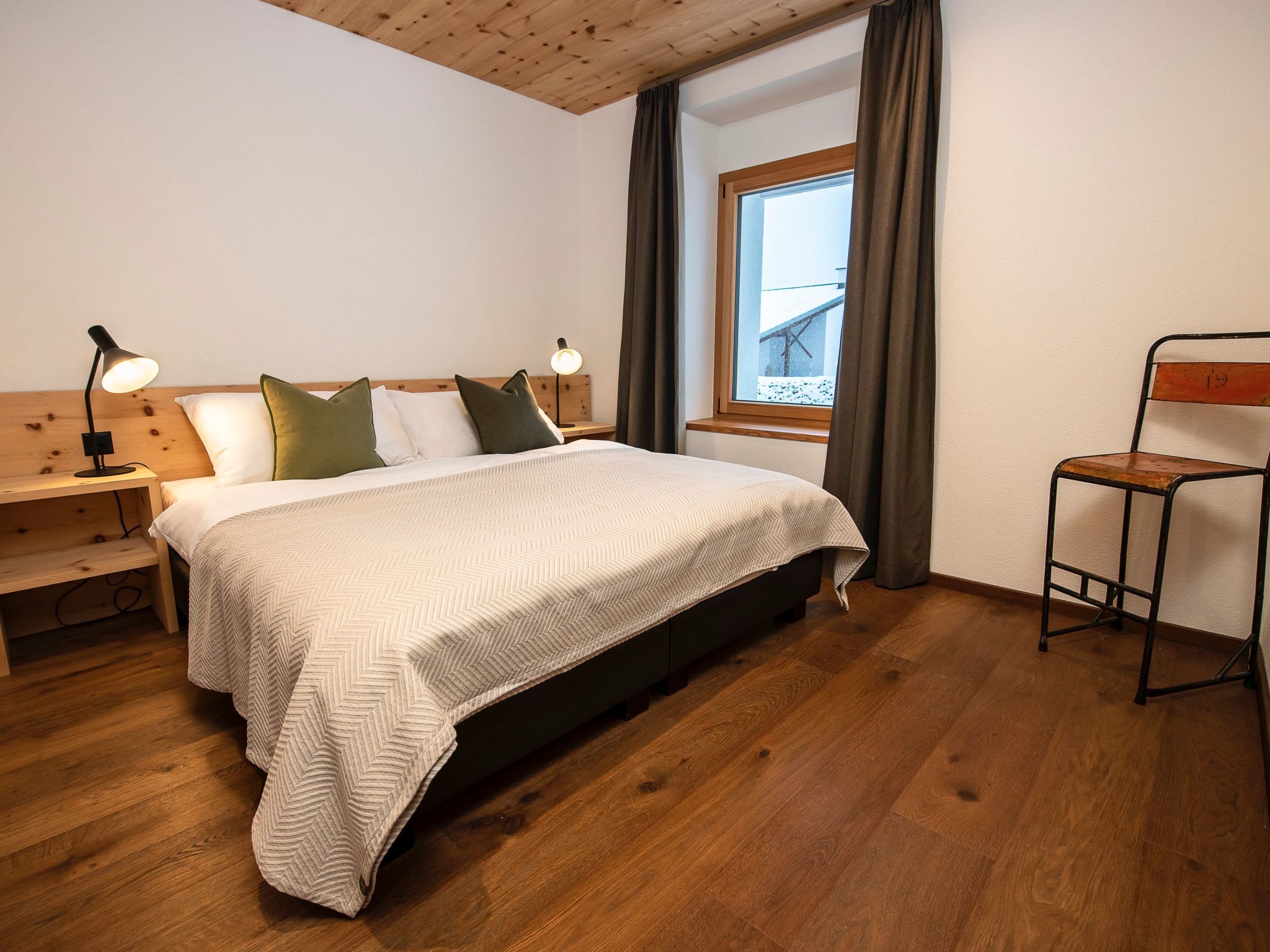 A bedroom with a bed, bedside tables, a chair, a window, and curtains.