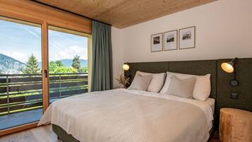 A bedroom with a large bed, a wooden ceiling, a view of greenery, and a balcony.
