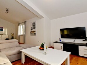 Ein modernes Wohnzimmer mit Sofa, Esstisch, Fernseher und Küchenzeile.