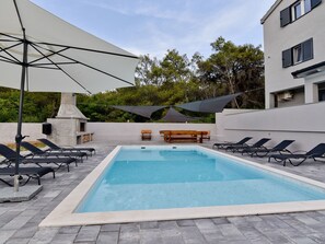 A rectangular swimming pool with a tiled deck, surrounded by lounge chairs and a barbecue area. - Vacation home  by Interhome (Crno)