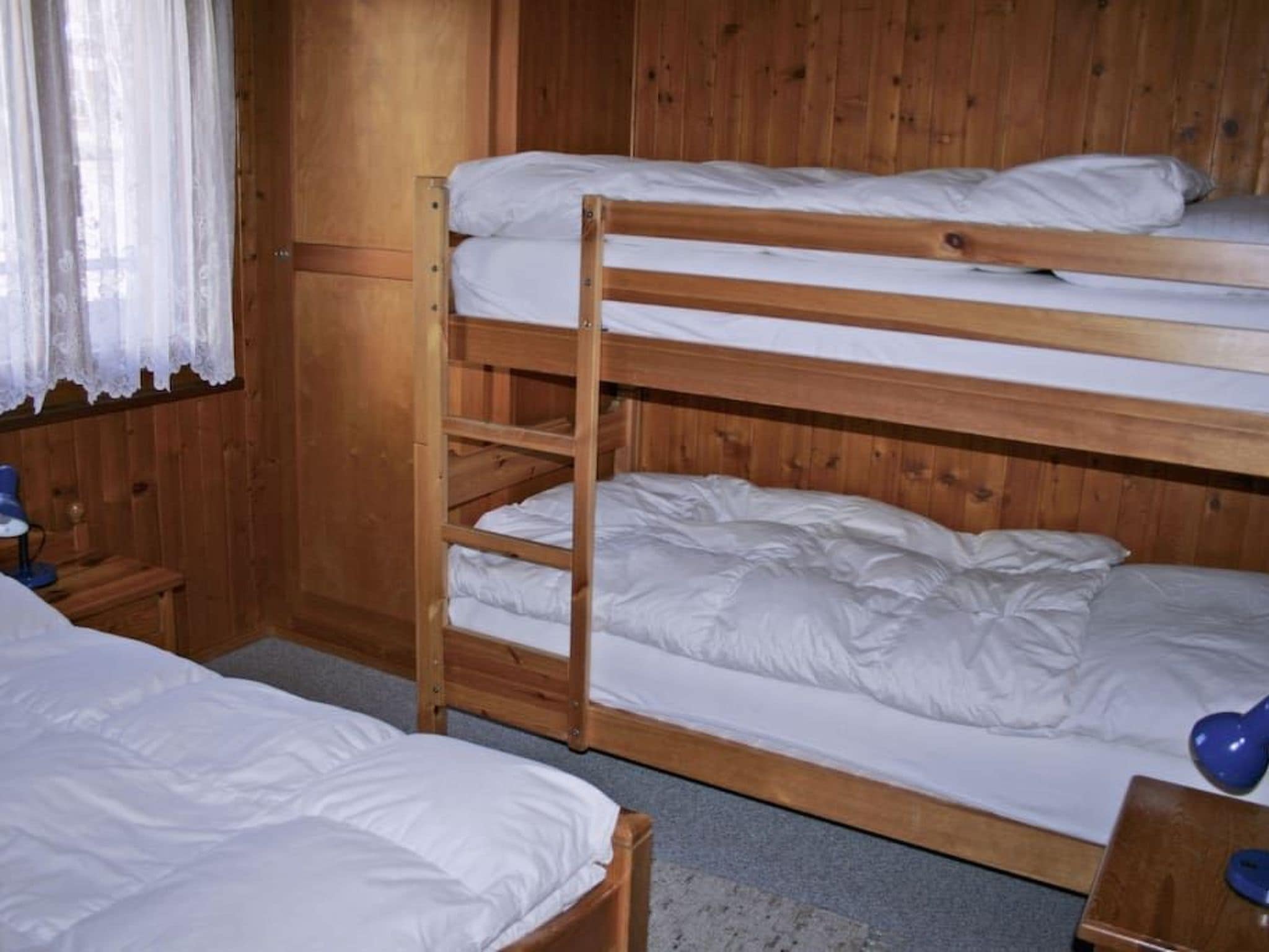 Habitación con literas de madera, una cama individual y una mesita con lámpara.