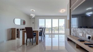 A modern living room with a dining area, large windows, and a flat-screen TV. - Pembroke 2BR Sea View Walk to Beach & Town (Pembroke)