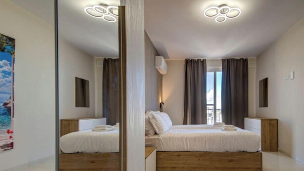 A modern bedroom with a large bed, bedside tables, a mirror, and a view of the sea. - Pembroke 2BR Sea View Walk to Beach & Town (Pembroke)