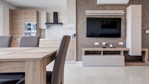 A modern kitchen with built-in appliances, a dining area with a wooden table and chairs, and a flat-screen TV mounted on the wall. - Pembroke 2BR Sea View Walk to Beach & Town (Pembroke)