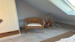 Habitació amb sostre inclinat, una cadira de vimetla, una planta en test i una porta blanca.
