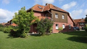 Una casa de dues plantes amb teulada inclinada, un petit porxo davanter i un jardí ben cuidat.