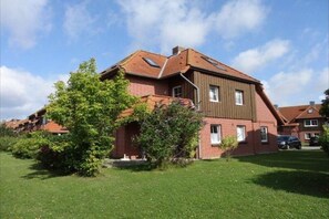A two-story house with a sloped roof, a small front porch, and a well-maintained lawn. - Ferienwohnung mit Balkon in Petersdorf (Petersdorf)