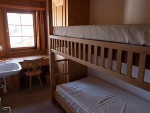 Une chambre avec un lit superposé, un bureau et une chaise, une fenêtre et un lavabo.