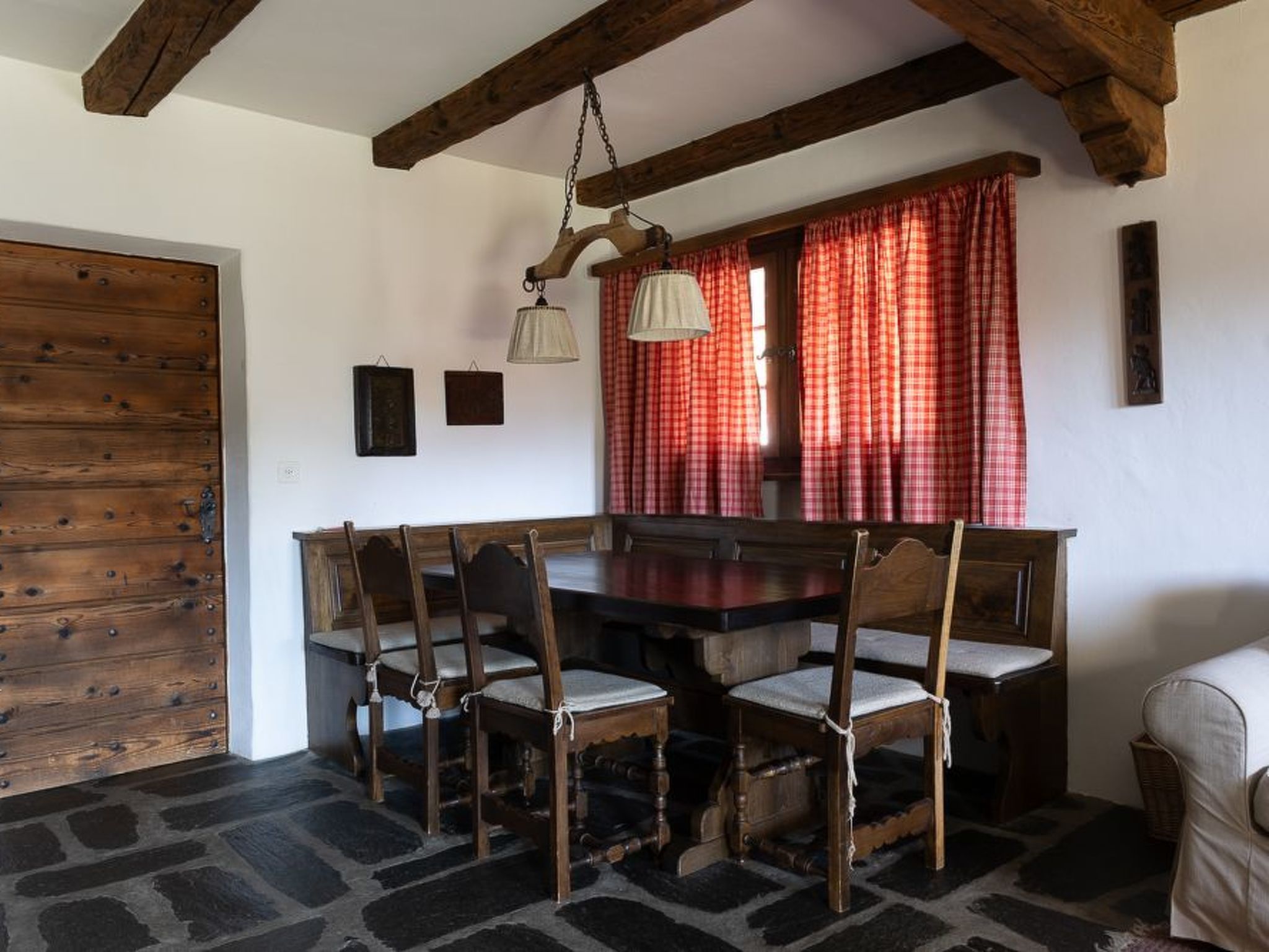 Ein rustikaler Essbereich mit einem Holztisch und -stühlen, Steinböden und einem Holzbalken an der Decke.