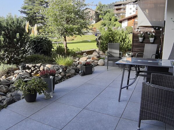 Un espace extérieur aménagé en patio, avec une table et des chaises, entouré de plantes en pot et de rochers.