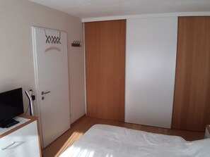Ein Schlafzimmer mit einem Bett, einem Schreibtisch mit Computer, einem Kleiderschrank und einer Tür mit Schlüsselloch.