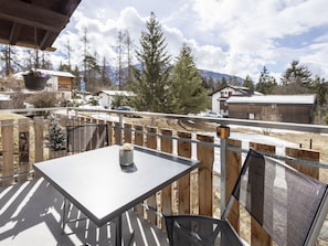 Eine Terrasse mit Tisch und Stühlen, mit Blick auf eine verschneite Landschaft mit Gebäuden und Bäumen.