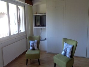 Ein Zimmer mit zwei grünen Sesseln, jeder mit einem Deer-Kissen. Ein Flachbildfernseher ist an der Wand über einem weißen Schrank angebracht.