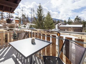 Eine Terrasse im Freien mit Tisch und Stühlen, mit Blick auf eine verschneite Landschaft mit Bäumen und Gebäuden.