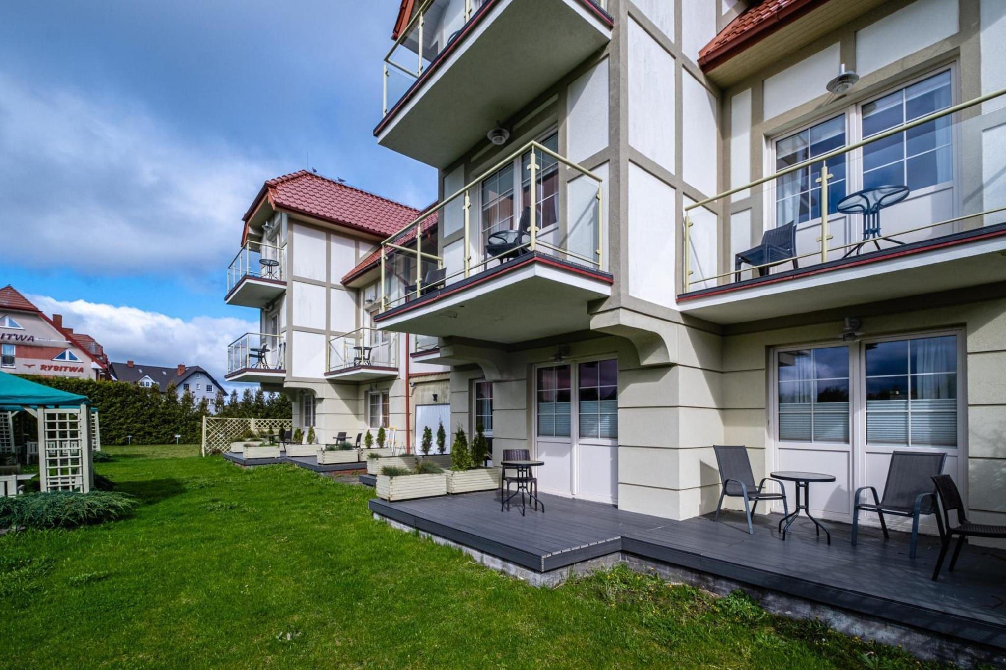 Ein mehrgeschossiges Wohngebäude mit Balkonen, einer gepflasterten Terrasse und Sitzgelegenheiten im Freien.