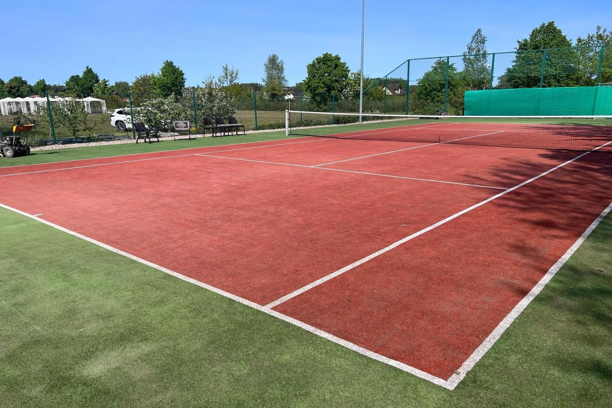 A tennis court with a green surrounding area and a white fence.