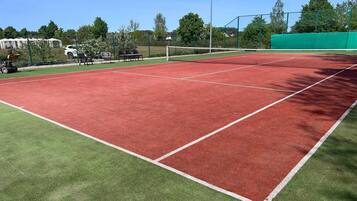 A tennis court with a green surrounding area and a white fence.
