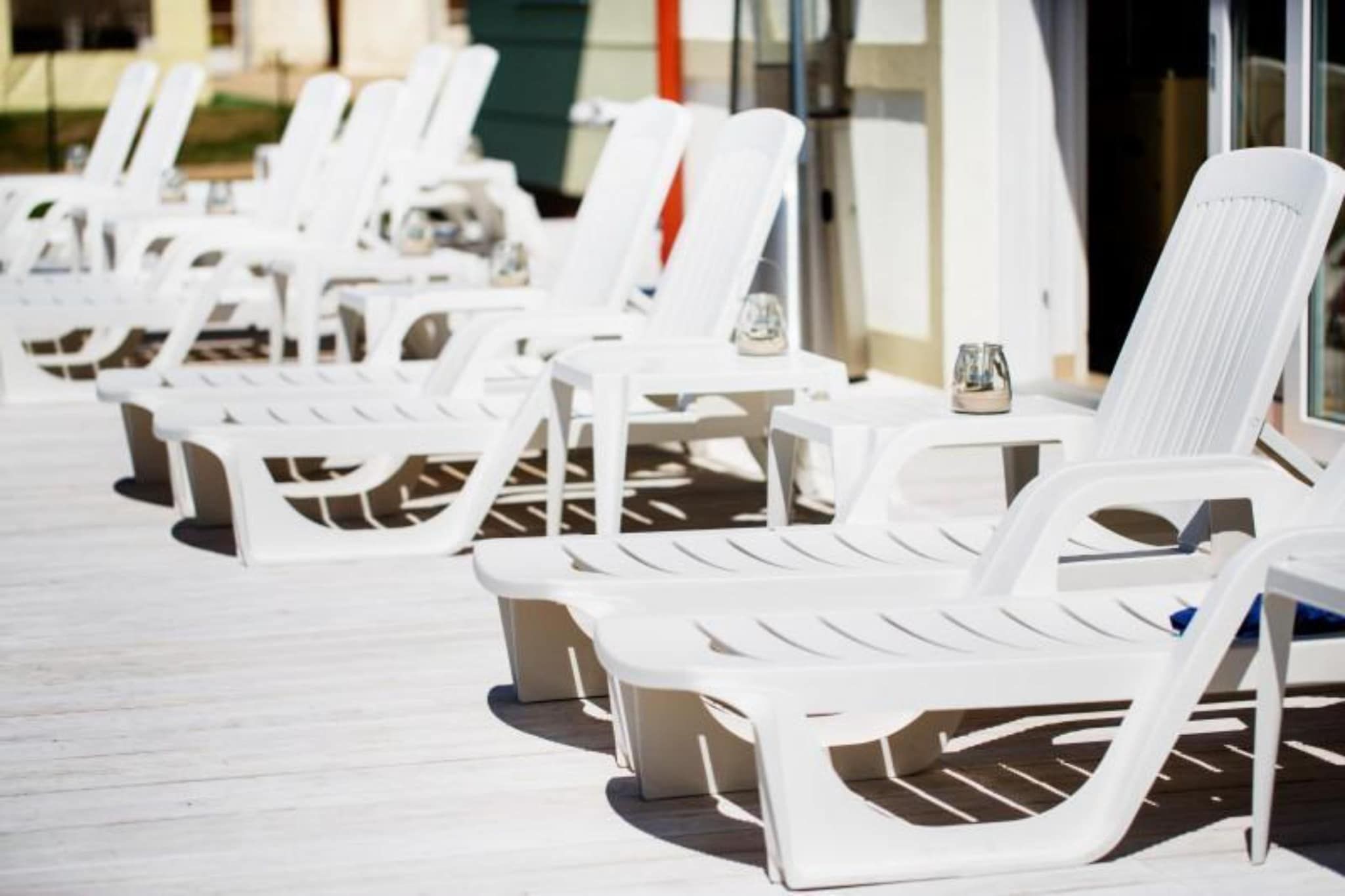 A row of white lounge chairs with tables, arranged on a wooden deck.