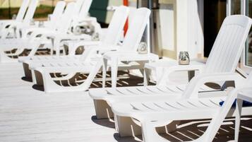 A row of white lounge chairs with tables, arranged on a wooden deck.