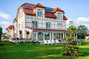 A multi-story building with a red-tiled roof, large windows, and a covered outdoor area with chairs and umbrellas. - Cozy and comfortable apartment for 2 people (Debki)