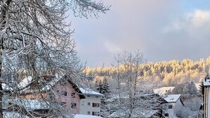 Lumipeitteinen maisema, jossa on rakennuksia, puinen aita ja kirkas taivas.