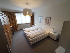 A bedroom with a bed, bedside tables, a radiator, curtains, and a hanging light fixture.